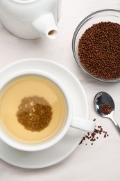 Photo of Cup of buckwheat tea, granules and teapot on white wooden table, flat lay