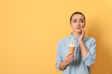 Emotional young woman with sensitive teeth and ice cream on color background. Space for text