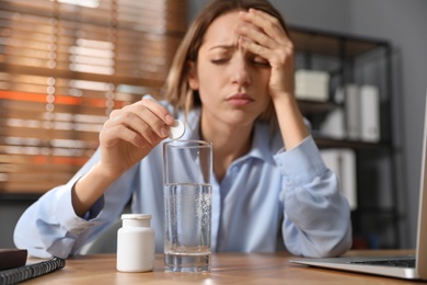 Woman putting medicine for hangover into glass of water in office, focus on hands