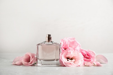Bottle of perfume with fresh flowers on light background