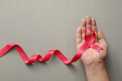 Man holding pink ribbon on grey background, top view with space for text. Breast cancer awareness concept