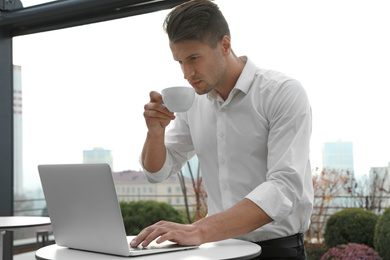Businessman with laptop and coffee in outdoor cafe. Corporate blog