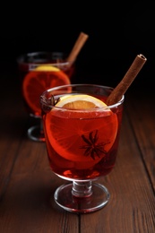 Glasses with red mulled wine on wooden table against dark background