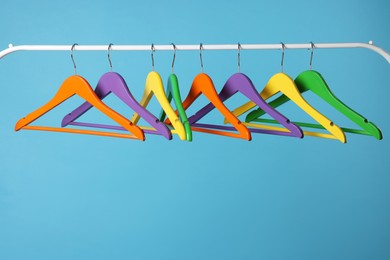 Bright clothes hangers on metal rail against light blue background