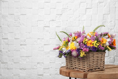 Photo of Wicker basket with beautiful wild flowers on table near white wall