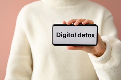 Woman holding smartphone with phrase DIGITAL DETOX on screen against pink background, closeup