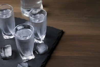 Shot glasses of vodka with ice cubes on wooden table. Space for text