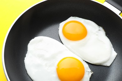 Tasty fried eggs in pan on yellow background, closeup