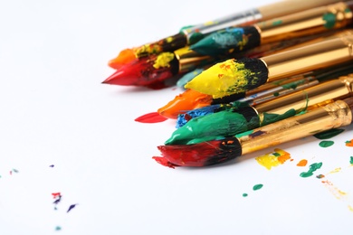 Brushes with colorful paints on white background, closeup. Space for text