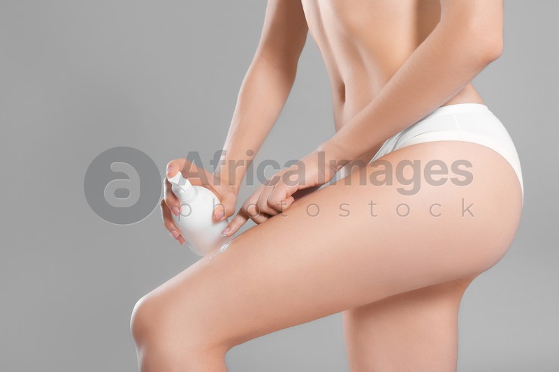 Young woman with bottle of body cream on color background
