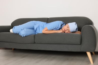 Photo of Tired young doctor sleeping on sofa indoors