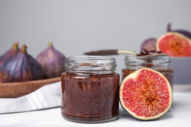 Photo of Glass jars of tasty sweet fig jam and fruits on white wooden table
