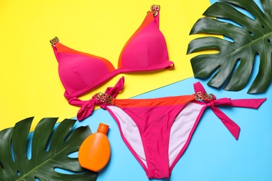Stylish women's swimwear, sunscreen and green leaves on color background, flat lay