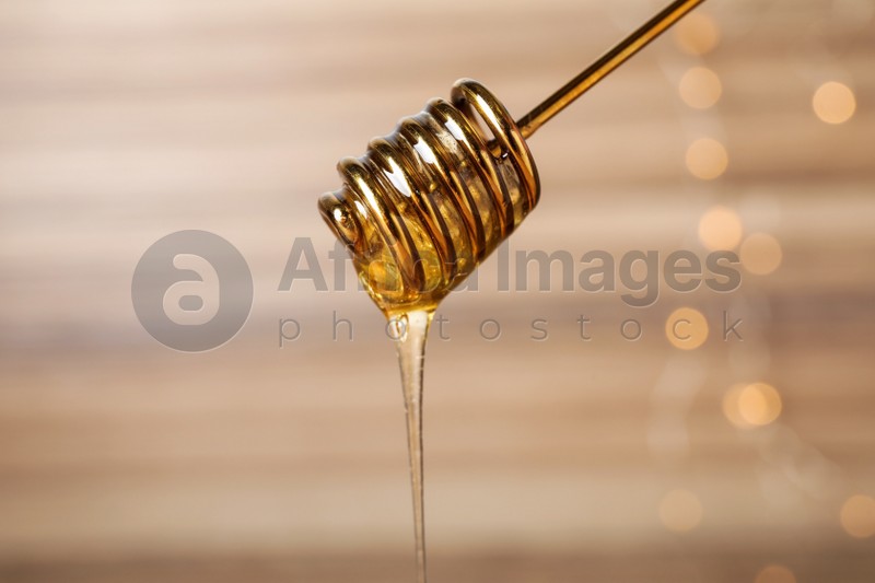 Photo of Dripping tasty honey from dipper on blurred background, closeup