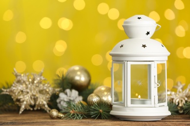 Christmas lantern with burning candle and festive ornaments on wooden table against blurred lights. Space for text