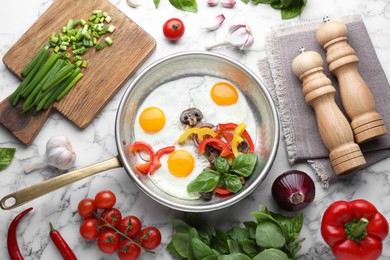 Tasty fried eggs with vegetables in pan and ingredients on white marble table, flat lay