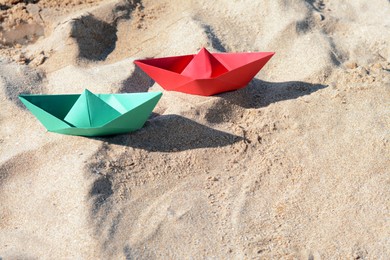 Photo of Two color paper boats on sandy beach, above view. Space for text