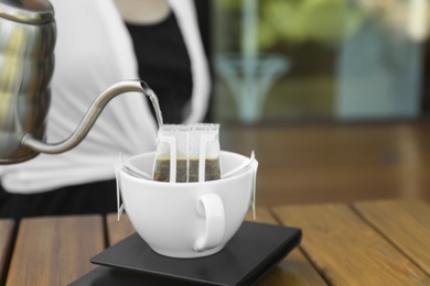 Woman pouring hot water into cup with drip coffee bag at wooden table, closeup