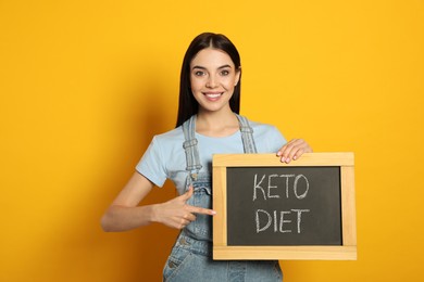 Happy woman holding chalkboard with words Keto Diet on yellow background