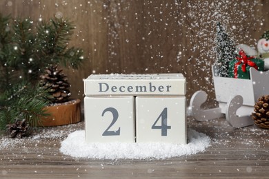 Photo of December 24 - Christmas Eve. Snow falling onto wooden block calendar and festive decor on table