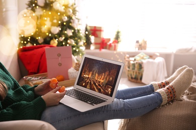 MYKOLAIV, UKRAINE - DECEMBER 25, 2020: Woman with tangerine watching Harry Potter and Philosopher's stone movie on laptop at home, closeup. Cozy winter holidays atmosphere