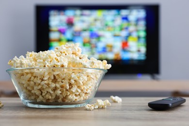 Bowl of popcorn and TV remote control on table indoors
