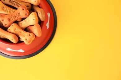 Photo of Bone shaped dog cookies in feeding bowl on yellow background, top view. Space for text