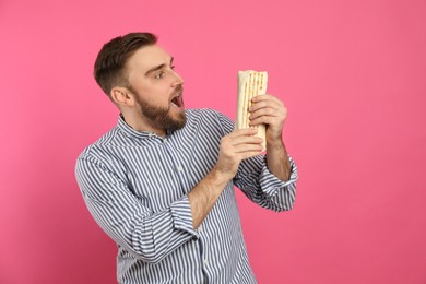 Photo of Emotional young man with delicious shawarma on pink background