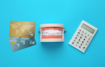 Educational dental typodont model, credit cards and calculator on light blue background, flat lay. Expensive treatment