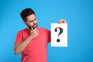 Emotional young man with question mark sign on light blue background