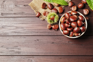 Fresh sweet edible chestnuts on brown wooden table, flat lay. Space for text