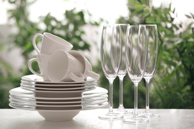 Photo of Set of clean dishware and champagne glasses on white table against blurred background