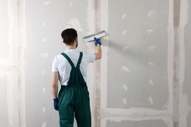 Worker in uniform plastering wall with putty knife indoors, back view. Space for text