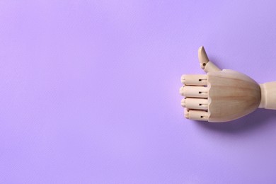 Wooden mannequin hand showing thumb up on lilac background, top view. Space for text