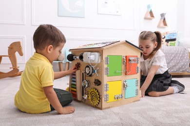 Little boy and girl playing with busy board house on floor in room