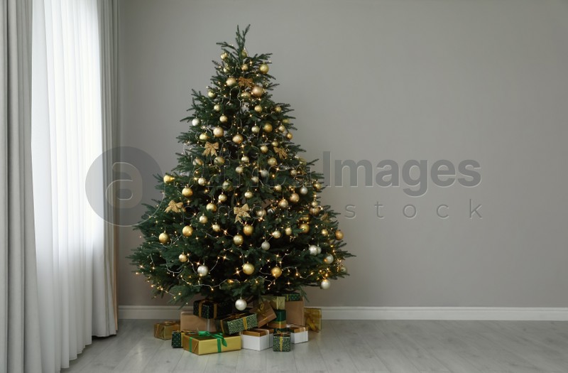 Beautifully decorated Christmas tree and gifts near grey wall indoors, space for text