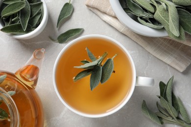 Flat lay composition with cup of sage tea and green leaves on light grey table