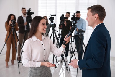 Professional young journalist interviewing businessman and group of video camera operators on background