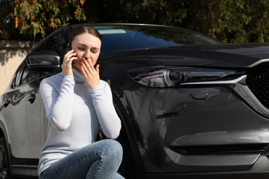 Photo of Stressed woman talking on phone near car with scratch outdoors