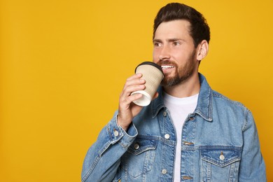 Photo of Handsome bearded man drinking from paper cup on orange background. Space for text