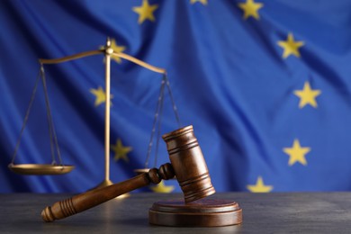 Wooden judge's gavel and Scales of justice on grey table against European Union flag