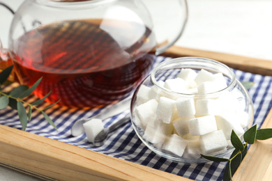 Refined sugar cubes in glass bowl and tongs on wooden tray