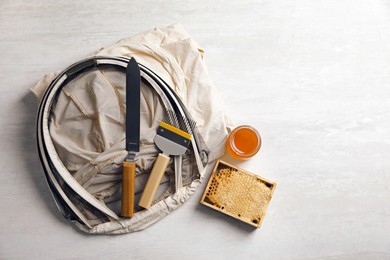 Different beekeeping tools and jar of honey on white table, flat lay. Space for text