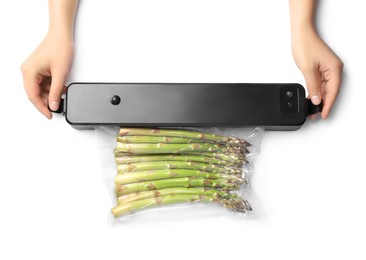 Woman using for vacuum packing with plastic bag of asparagus on white background, top view