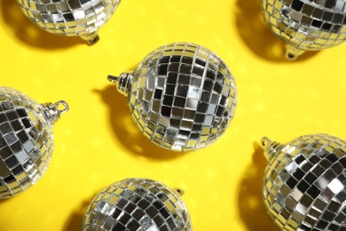 Shiny disco balls on yellow background, flat lay