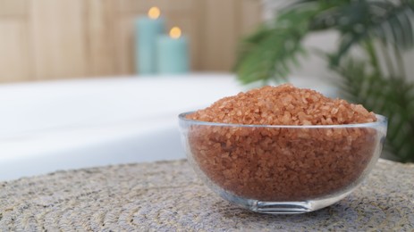 Glass bowl of bath salt on wicker mat in bathroom, closeup. Space for text