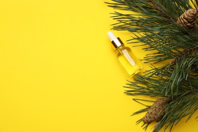 Glass bottle of essential oil and pine branch with cones on yellow background, flat lay. Space for text