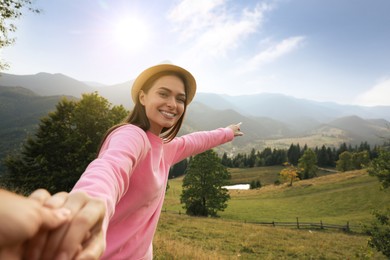 Photo of Young woman holding boyfriend's hand in mountains, space for text