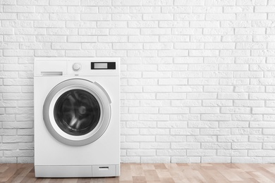 Modern washing machine near brick wall in empty laundry room, space for text