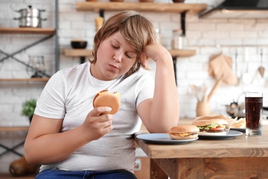 Overweight boy at table with fast food in kitchen
